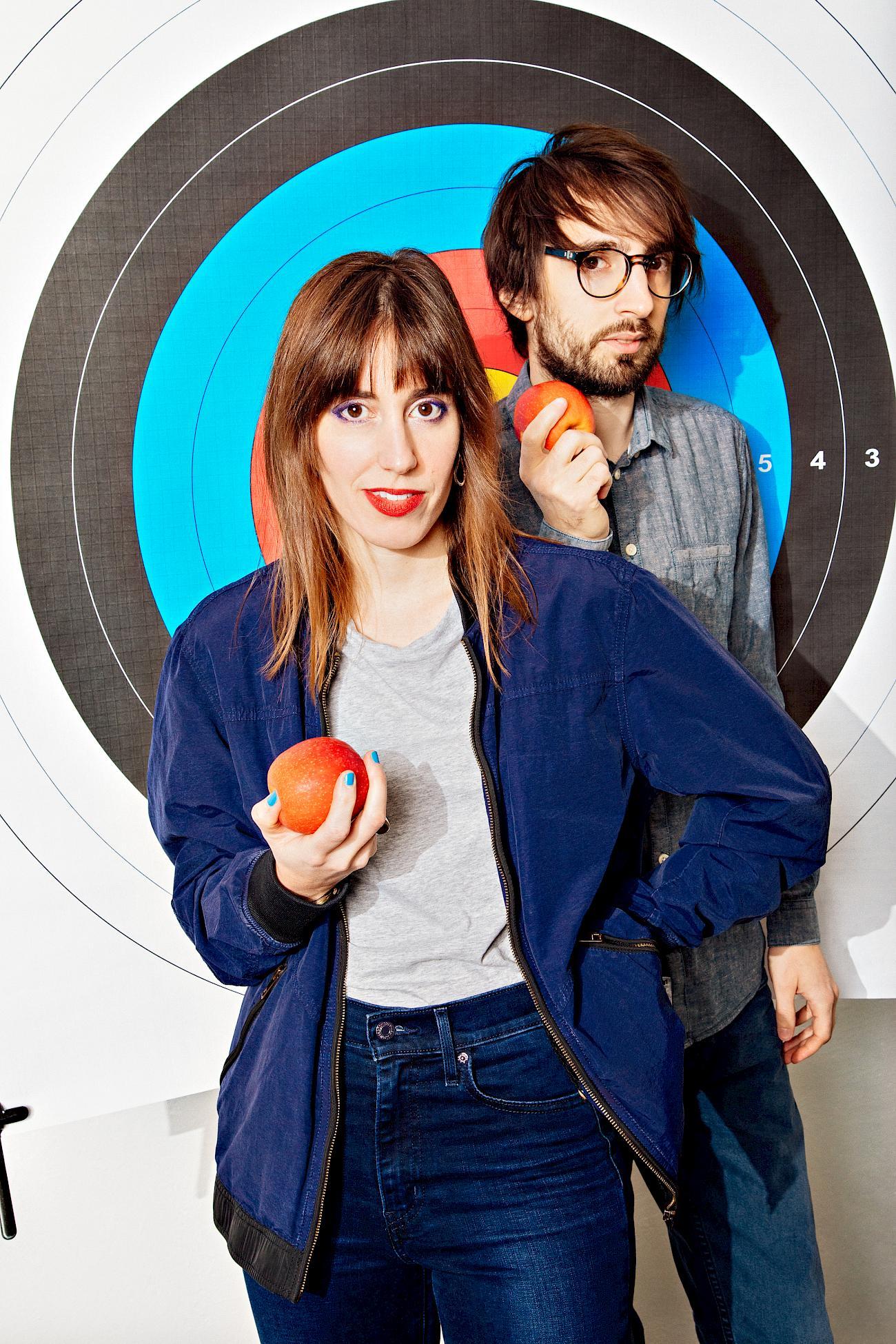 Maya & Daniele in front of an archery target holding an apple