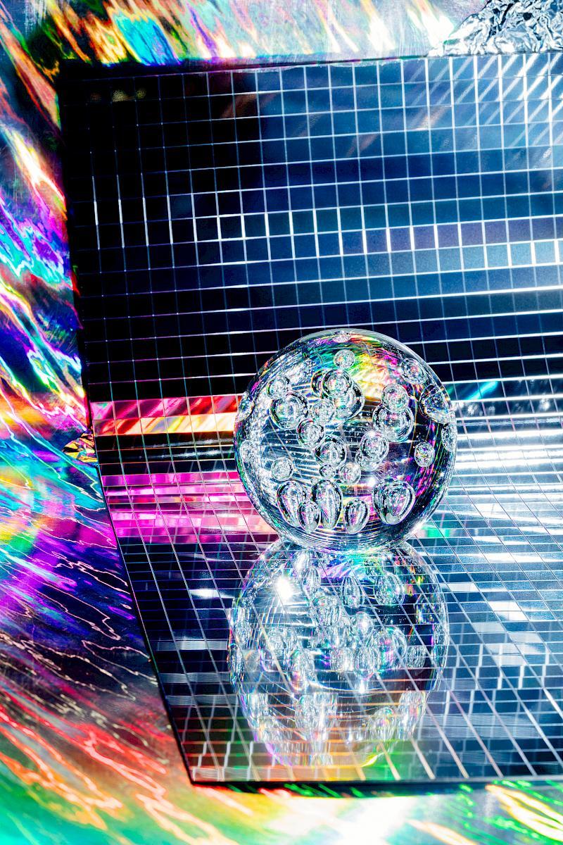 A glass sphere on a checkered disco mirror on a rainbow background