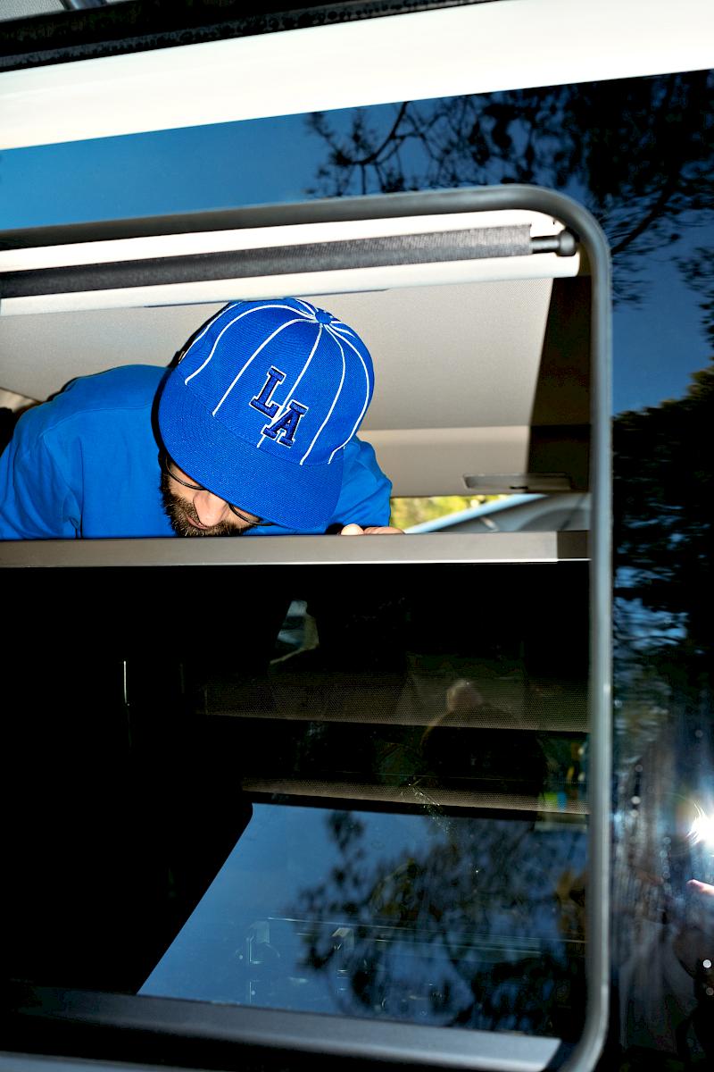 Man with a blue t-shirt and LA baseball cap inside a van