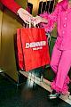 A man hands over a Denner groceries bag to a lady in a hot pink party pyjama with detachable feathers