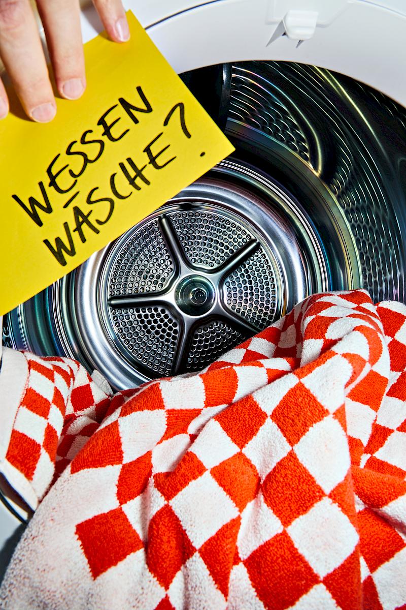 Baina roman pool towel in a washing machine with a hand holding a yellow post-it