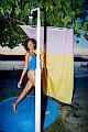 A woman wearing a blue swimsuit standing under a outdoor shower with a colourful SULA x Micasa curtain behind her