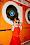 A child wearing a red dress and oversized green sunglasses poses in front of bright orange laundromat dryers