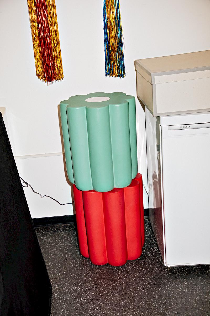 Two stacked flower-shaped stools in mint green and red displayed inside the artist's studio